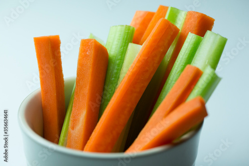 close up filled frame isolated shot of party snack food. A white bowl of crunchy orange carrot and juicy green celery sticks on a white background