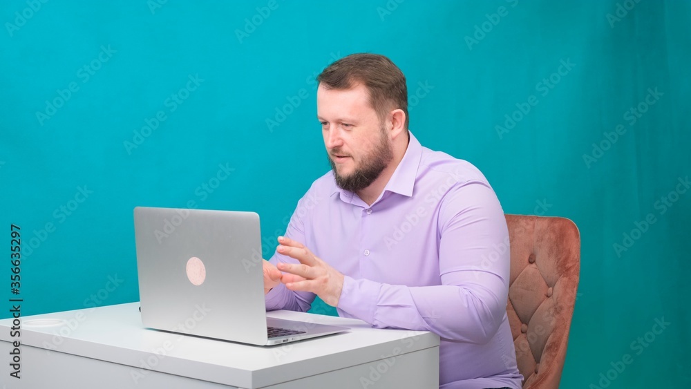 Young happy businessman holds a conference meeting at a laptop on a green screen. Portrait of a male talking man looking into his laptop. Man working at his desk in the office Young happy businessman holds a conference meeting at a laptop on a green screen. Portrait of a male talking man looking into his laptop. Man working at his desk in the office