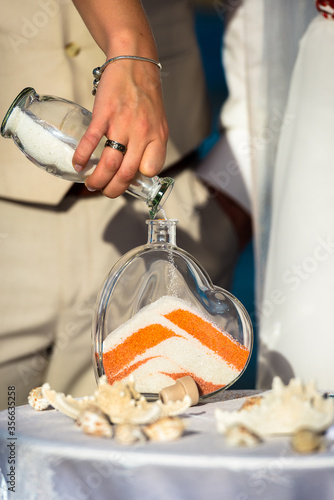 Ηand holding the bottle with white sand. Pour from one bottle to another with white and orange powder sand. photo