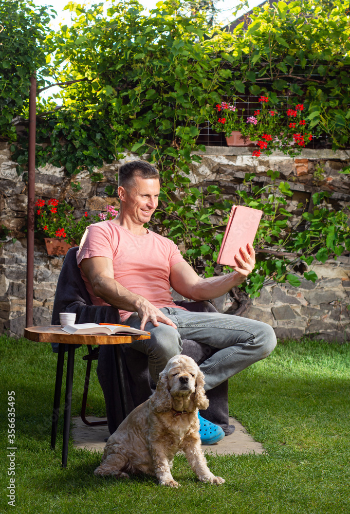 Obraz premium Handsome man relaxing on a chair and using tablet pc in the garden