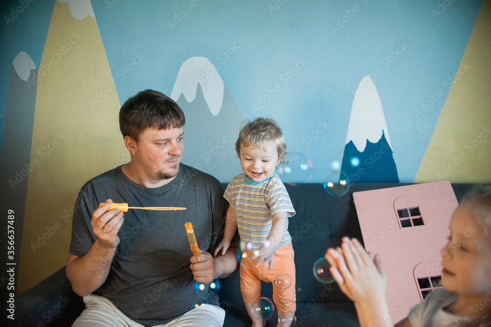  Dad plays soap bubbles at home with his children. dad plays at home with three children: a boy and girls, brother and sisters