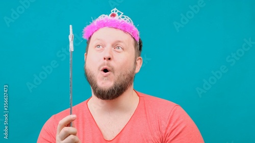 Cute bearded freaky man in a pink T-shirt with a deadema on his head dreams with a magic wand in his hand. A funny wizard joke to make and fulfill a wish. photo