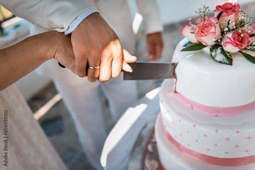 Bride and a groom are cutting their wedding cake on wedding banquet. Hands cut the cake decorated with roses. Bride and a groom are cutting their wedding cake on wedding banquet. Hands cut the cake decorated with roses.