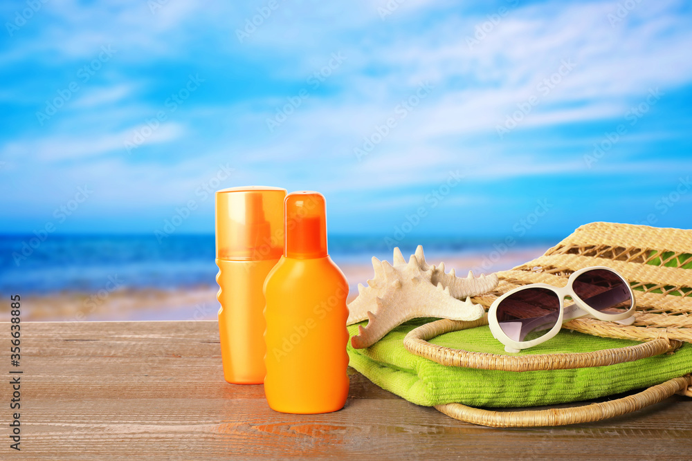 Set of sun protection products and stylish accessories on wooden table near sea Set of sun protection products and stylish accessories on wooden table near sea