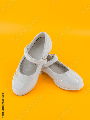 Pair of white baby lacquered girls shoes at yellow background