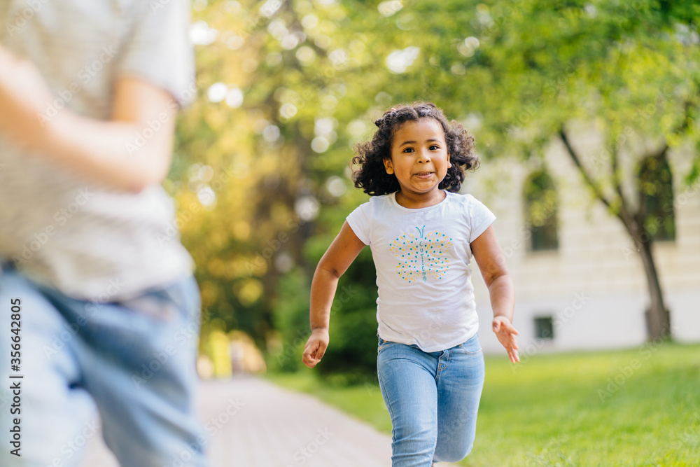 Two happy little kids having fun while running through the grassy field and racing against each other on the track in city summer park. Two happy little kids having fun while running through the grassy field and racing against each other on the track in city summer park.