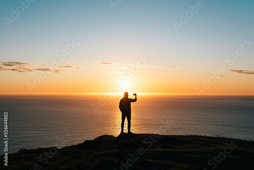 Silhouette of a young man taking pictures of sunset