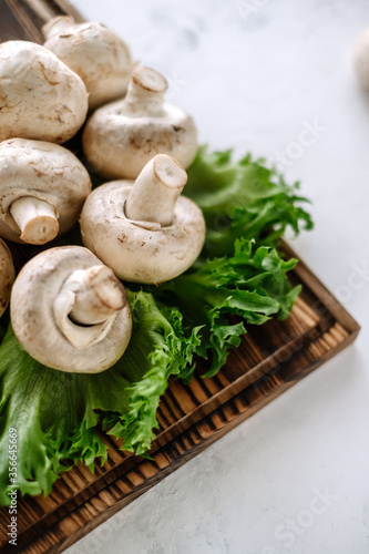 Champignon mushrooms on a wooden board with greens, close-up.