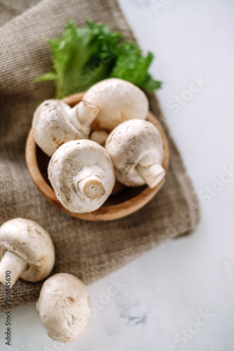 Champignon mushrooms in a wooden bowl with herbs on the table, close-up.