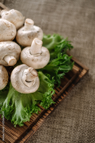 Champignon mushrooms on a wooden board with greens, close-up.