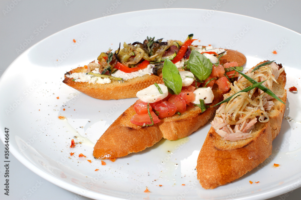 Italian bruschetta with salmon, tuna, mozzarella and grilled vegetables on a white plate