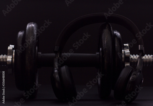 Black metal dumbbell for fitness with headphones, on a black background.