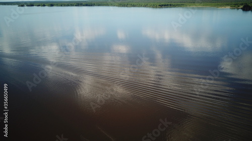 Aerial view of river Kama, Perm krai, Russia. Rural landscape from above, water waves, cloud reflection in water, trees on the coast, summer sun day. Copy space.