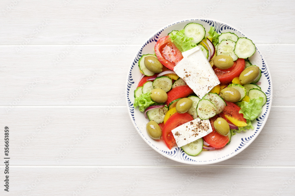 Greek salad with feta cheese, tomatoes, cucumbers, lettuce, olives and spices. Traditional greek cuisine. White rustic wooden table