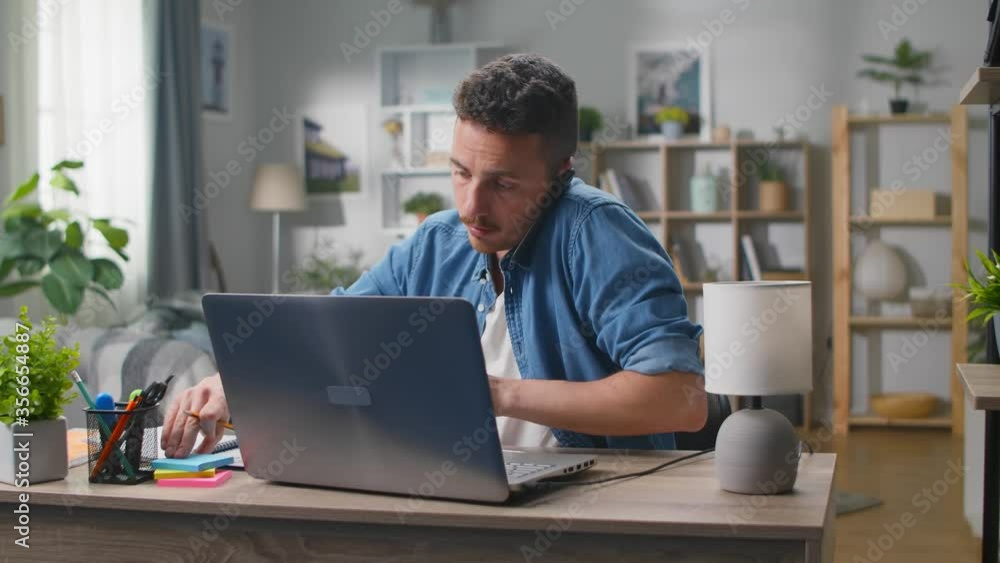 Young businessman talking on a smartphone at a workplace at home in the living room Young businessman talking on a smartphone at a workplace at home in the living room