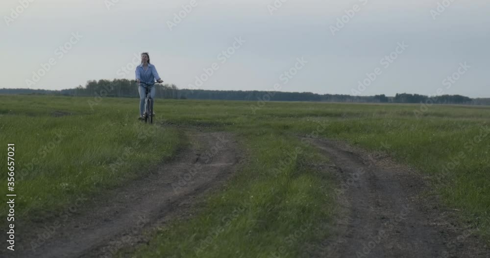 Girl Rides Bicycle on Field on Country Road. Enjoys Ride. Looks around. Nature. Countryside. Got out of city. Sun is setting. Returns Home. Summer. Wonderful Weather. Old Bicycle. Vintage Girl Rides Bicycle on Field on Country Road. Enjoys Ride. Looks around. Nature. Countryside. Got out of city. Sun is setting. Returns Home. Summer. Wonderful Weather. Old Bicycle. Vintage