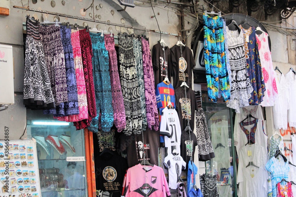 skirts of various colors and motifs and black t-shirts and soccer teams hanging outside a clothing store in the historic center of Palermo in Italy