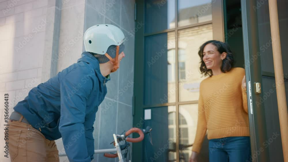 Happy Food Delivery Man on a Bike Delivers Restaurant Order to a Beautiful Female Customer. Courier Delivers Takeaway Lunch to Gorgeous Girl in Modern City District Office Building. Slow Motion Happy Food Delivery Man on a Bike Delivers Restaurant Order to a Beautiful Female Customer. Courier Delivers Takeaway Lunch to Gorgeous Girl in Modern City District Office Building. Slow Motion