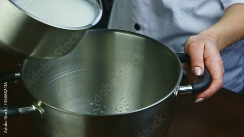 slow motion closeup woman pours milk from small saucepan into tall metal bowl