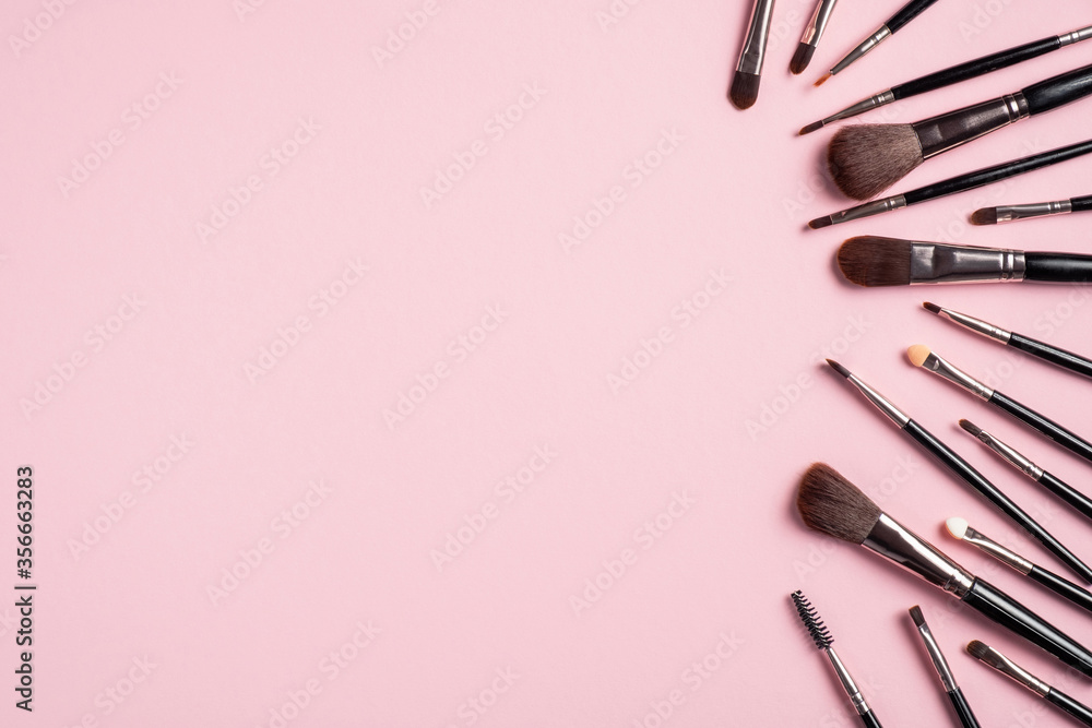 Fototapeta Set of different black makeup brushes on pink background. Flat lay, top view. Makeup shop banner design.