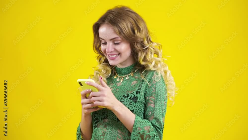 Young american girl using mobile phone, typing sms message. She scrolls through social networks over yellow background. Young american girl using mobile phone, typing sms message. She scrolls through social networks over yellow background.