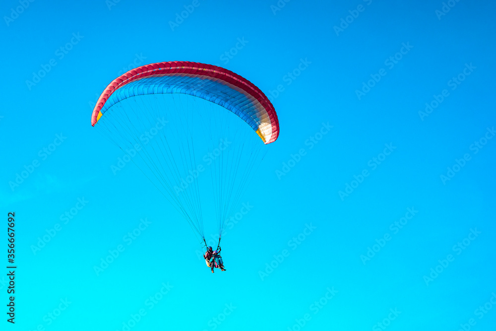 Doubles paragliding against a clear blue sky. A multi-colored papaplan flies in the clear sky closeup. Doubles paragliding against a clear blue sky. A multi-colored papaplan flies in the clear sky closeup.