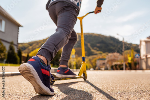 A teenage boy rides a scooter. Right foot in a sneaker close-up. Bottom view. Empty street in Sunny weather in the background. Concept of youth activity, sports and recreation