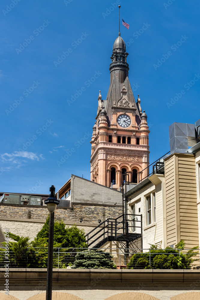 The historic city hall of Milwaukee, Wisconsin towers over city buildings and a rooftop patio with greenery. The historic city hall of Milwaukee, Wisconsin towers over city buildings and a rooftop patio with greenery.