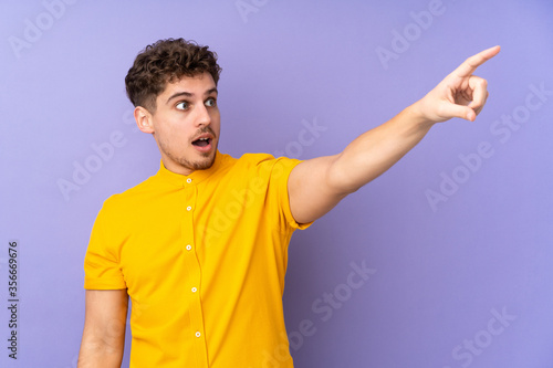 Caucasian man isolated on purple background pointing away