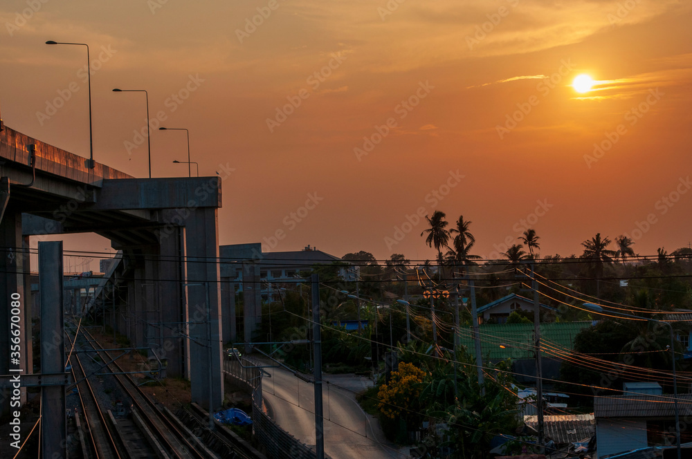 Railway station against beautiful sky at sunrise. Urban landscape with railroad under expressway, colorful of environment with sunrise, trees and green grass. Railway junction.Sun, sky, railroad and e Railway station against beautiful sky at sunrise. Urban landscape with railroad under expressway, colorful of environment with sunrise, trees and green grass. Railway junction.Sun, sky, railroad and e