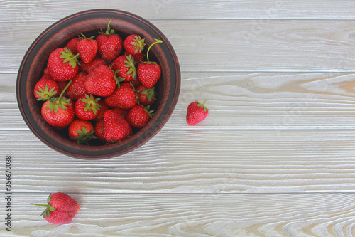 fresh strawberries in a ceramic bowl on a white wooden background.