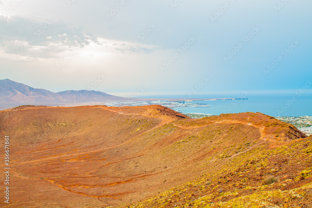 Fototapeta premium panoramic view of Volcano Montana Roja de Playa Blanca, Lanzarote, Spain. One of the most popular volcano in Canary Islands and the total view of the village in the south with white houses. 