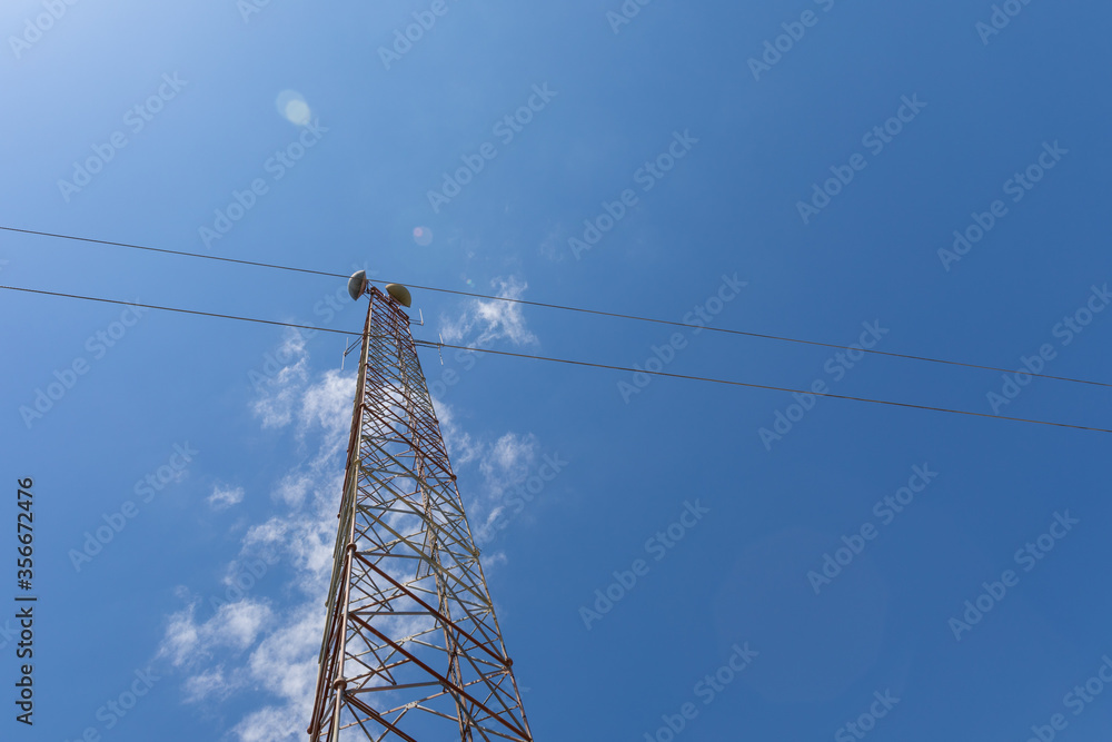 Extremely tall telecommunications tower seen from below with microwave antennas, silhouetted against a beautiful blue sky with sparse clouds, copy space, horizontal aspect Extremely tall telecommunications tower seen from below with microwave antennas, silhouetted against a beautiful blue sky with sparse clouds, copy space, horizontal aspect