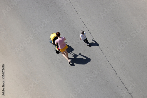 Young woman with two children crossing the street, top view. Concept of motherhood, road safety, single mom with kids at summer