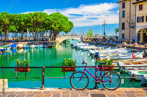 Bicycle bike near fence of old harbour Porto Vecchio with motor boats on turquoise water and Venetian bridge in historical centre of Desenzano del Garda town, blue sky, Lombardy, Northern Italy photo
