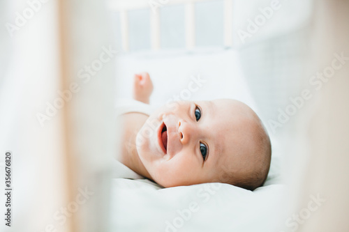 Little cute adorable boy is in the nursery with a white crib and laughs