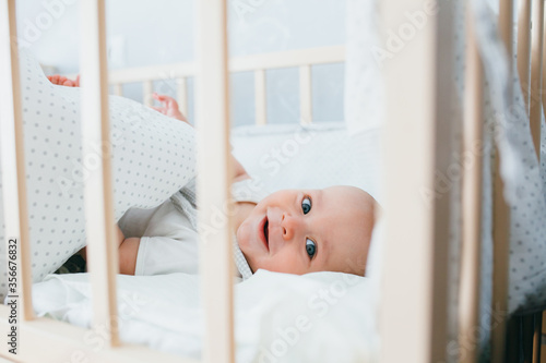 Little cute adorable boy is in the nursery with a white crib and laughs
