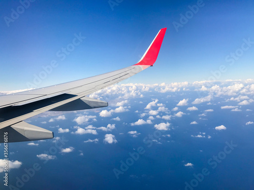 Airplane wing caught during flight between heavily thick white clouds and blue sky from window during fly-by on ocean.