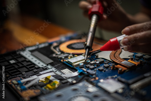 Close-up hand technician repairing broken laptop notebook computer with electric soldering Iron