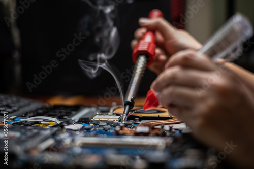 Close-up hand technician repairing broken laptop notebook computer with electric soldering Iron