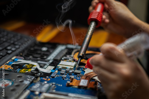 Close-up hand technician repairing broken laptop notebook computer with electric soldering Iron