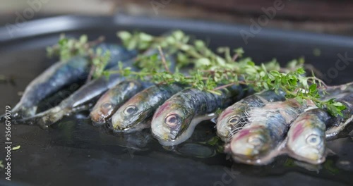 Grilled sardines with addition of fresh herbs, lemon and spices on a wooden background. Grilled seafood, barbecue