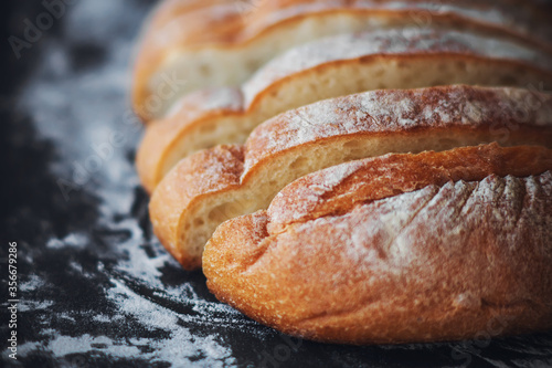 Foto Fresh, warm, sliced wheat bread lies on a dark baking tray strewn with white crumbly flour