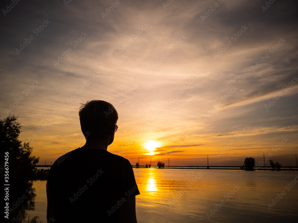 Silhouette of a man with a short haircut on the background of the lake in the light of the setting sun. Copyspace. Warm shades.