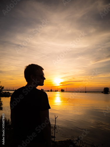 Silhouette of a man with a short haircut on the background of the lake in the light of the setting sun. Copyspace. Warm shades. photo