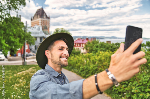 A nice tourist man with cheateau frontenac on the back taking a selfie photo