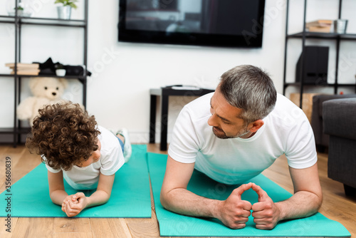bearded father and curly son exercising on fitness mats