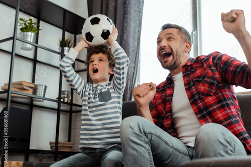 excited kid holding football while watching championship with father