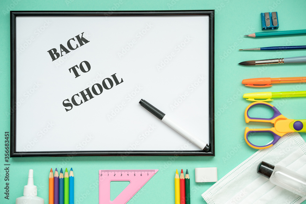 Back to school in a new reality, a medical mask, a sanitizer, stationery: pencils, pen, brush, glue, scissors, a ruler. Text back to school, flat lay. Back to school in a new reality, a medical mask, a sanitizer, stationery: pencils, pen, brush, glue, scissors, a ruler. Text back to school, flat lay.