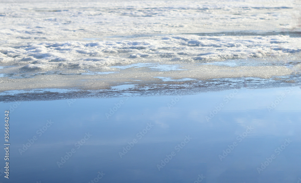 Melting of ice and snow on the lake in spring. Snow and ice in the reservoir. Reflection of the sky in the lake. Selective focus. Landscape